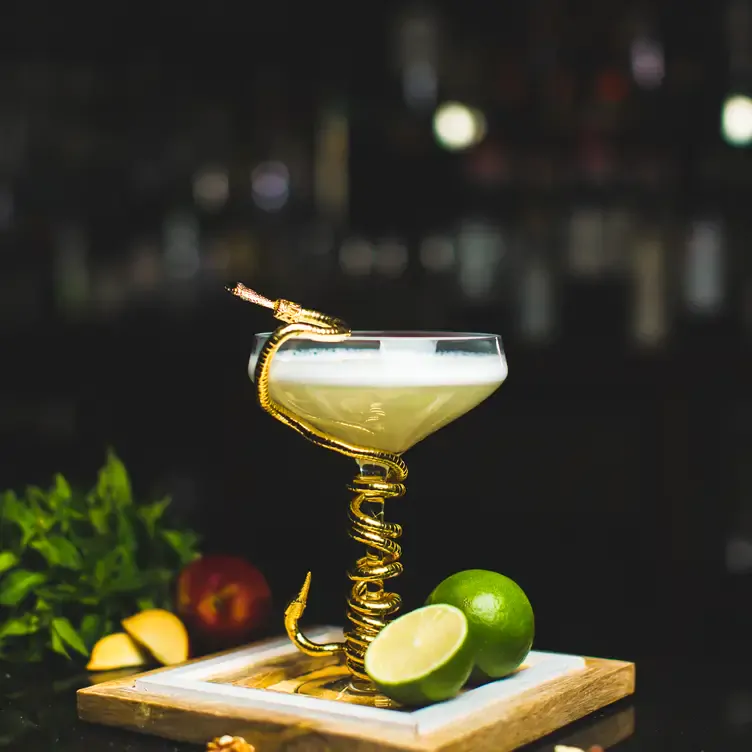 A cocktail decorated with a gold snake, accompanied by lime at Asha’s Birmingham, one of the best date night restaurants in Birmingham.