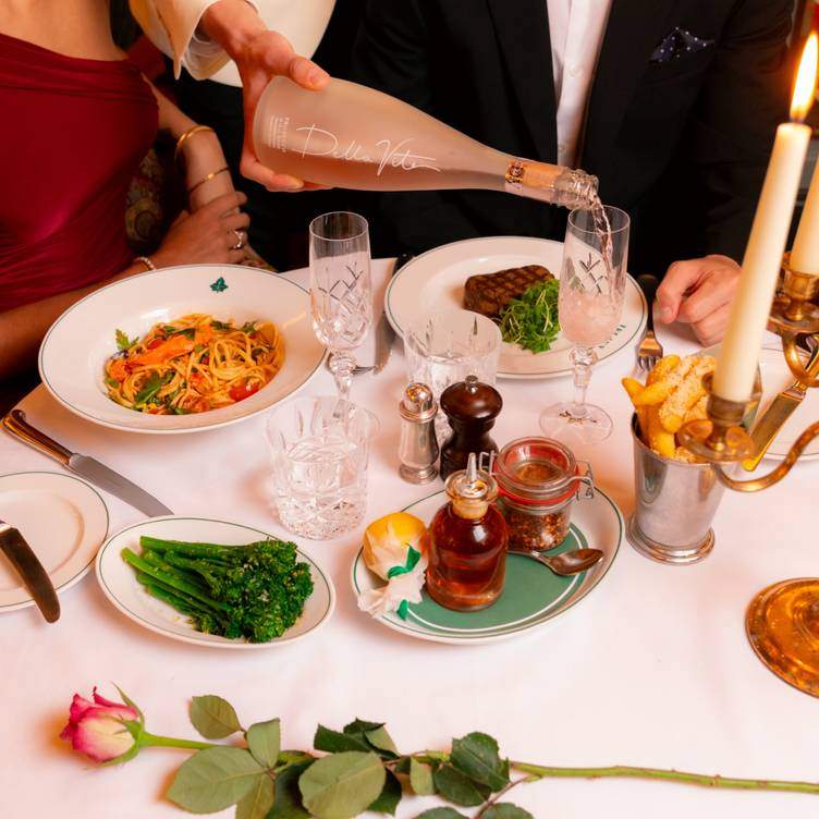 A waiter poors wine at a table featuring spaghetti and meat dishes and a rose at The Ivy Temple Row, one of the best romantic restaurants in Birmingham