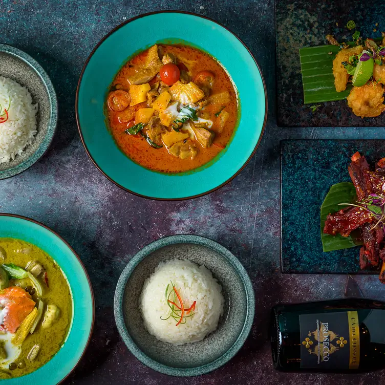 Two dishes of Thai curry along with rice sit on a table with a bottle of prosecco at Siamais, in Birmingham.