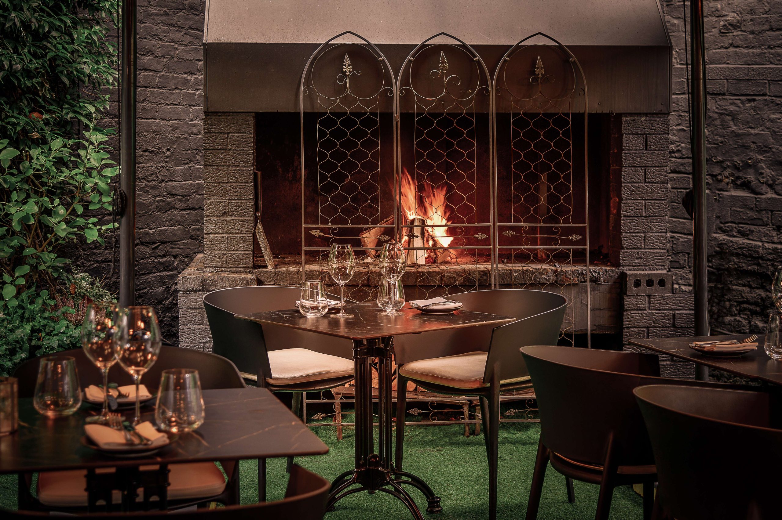 A trio of tables set with plates and wine glasses frame an open fireplace at Gaucho, a restaurant in London.