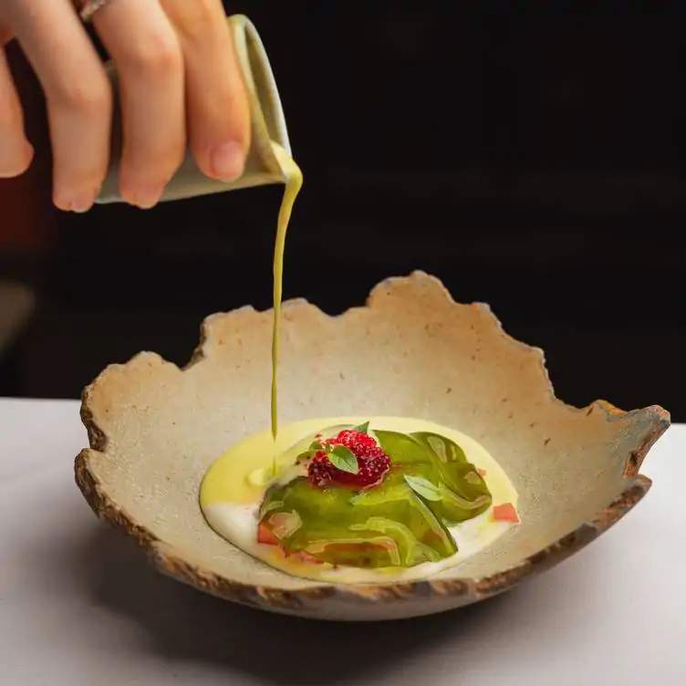 A waiter poors cream into a bowl featuring and Indian dish at Benares, one of the best Indian restaurants in London