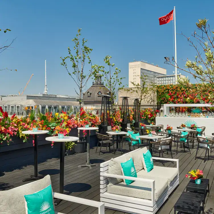 The sunny rooftop terrace at Aqua Nueva, with white banquettes, tables, flowers and a high red flag.