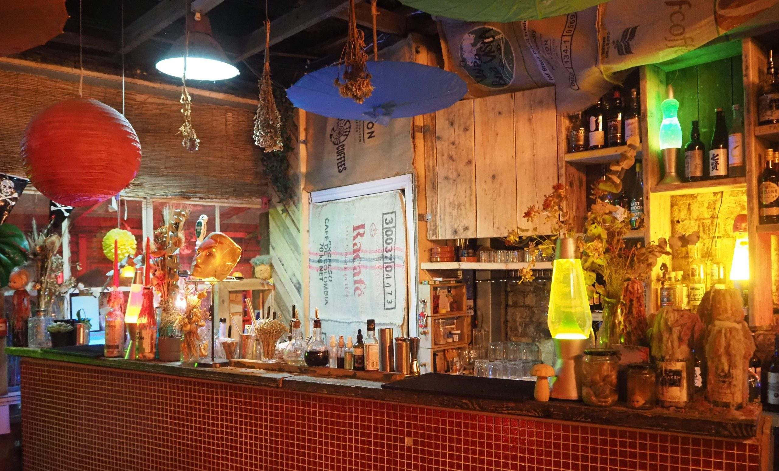 An image of colourful interiors of Love Shack, a restaurant in London, featuring wooden floors, a large library, red lights, and hanging paper lanterns and umbrellas.