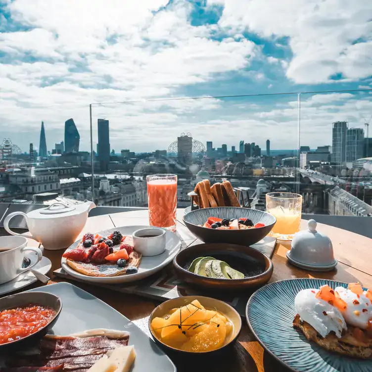 A spread of brunch dishes with views over London in the background at Radio Rooftop, one of the best outdoor restaurants in London