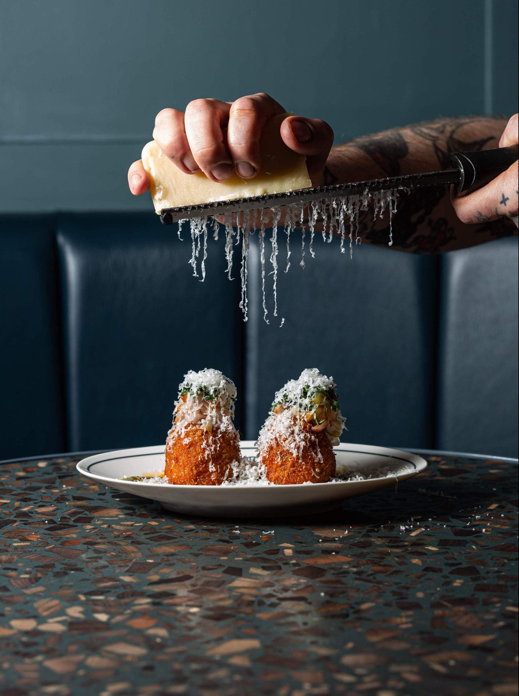 A chef grates cheese onto a plate of croquettes at The Black Grape, a restaurant in Edinburgh