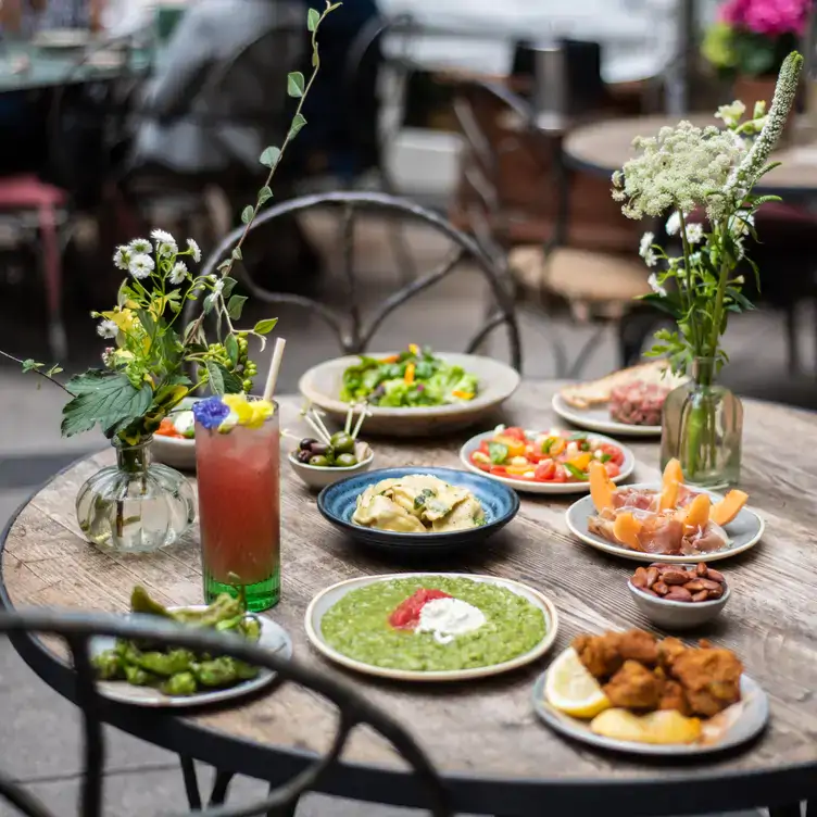 A spread of dishes and cocktails with flower bouquets at La Goccia, a restaurant in London