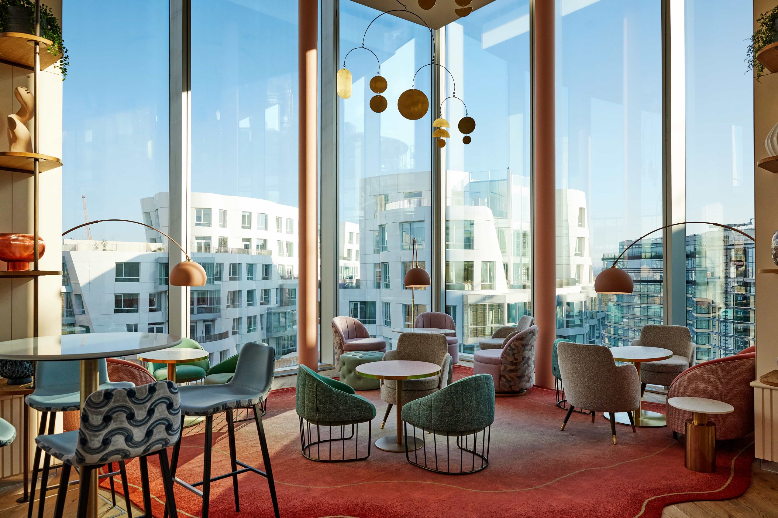 A modern sunlit dining room at the London restaurant JOIA featuring large floor-to-ceiling windows showing the Battersea skyline.