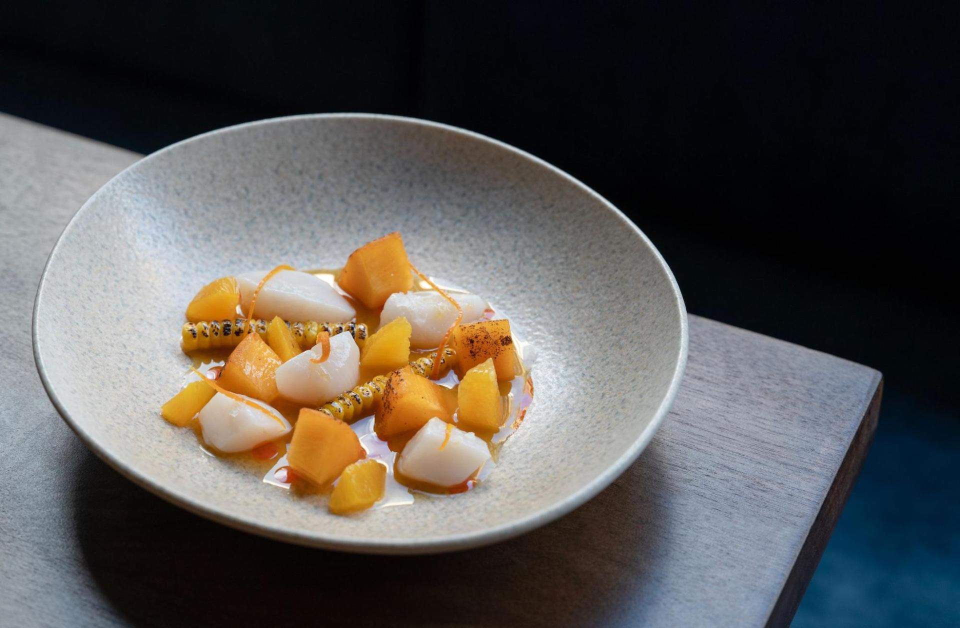 A ceramic bowl of orange and white seabass aguachile on a dark wooden table at London restaurant Zapote.