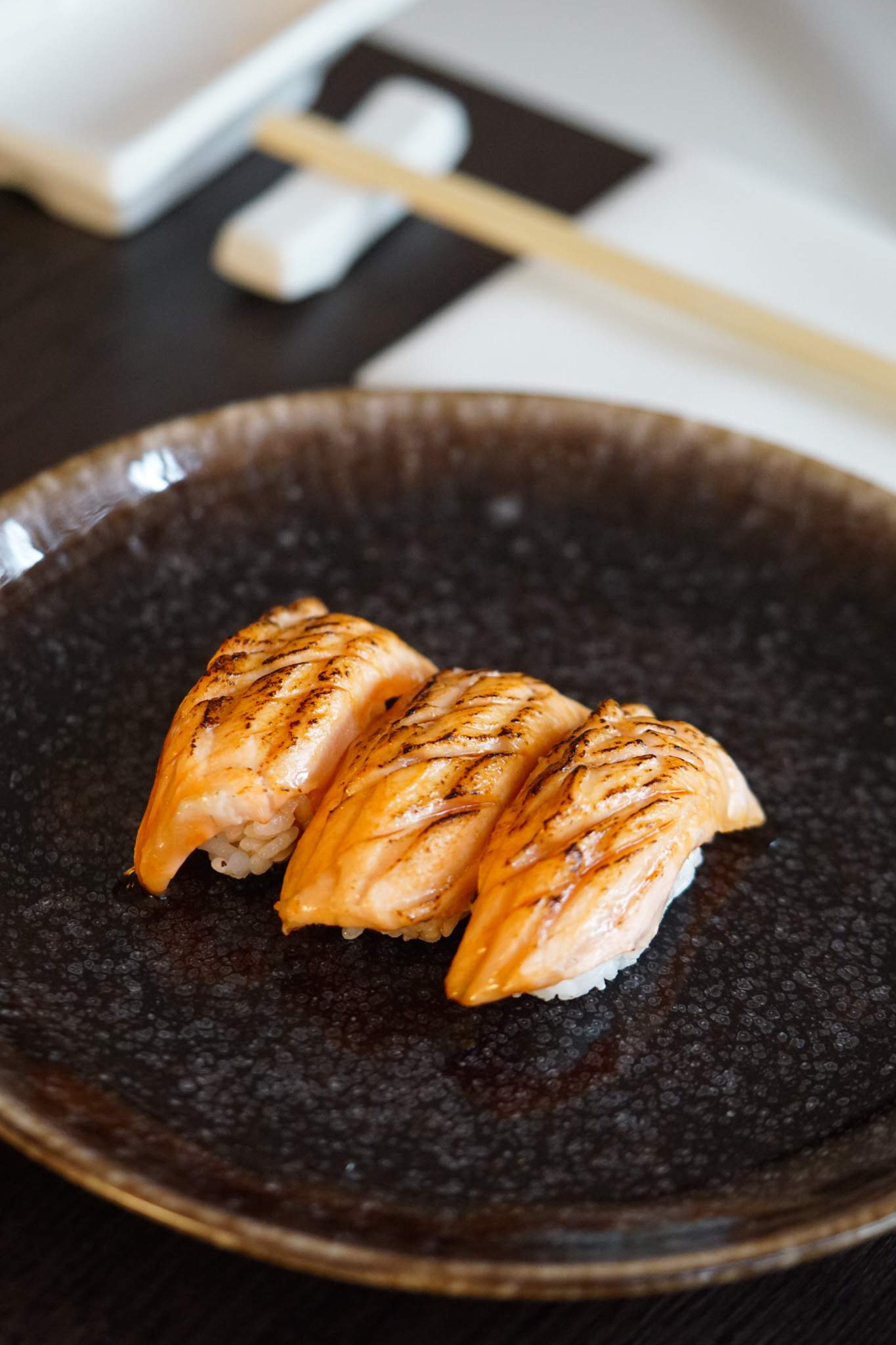 Three salmon nigiris on a black plate at Gaijin Sushi, a restaurant in Birmingham.