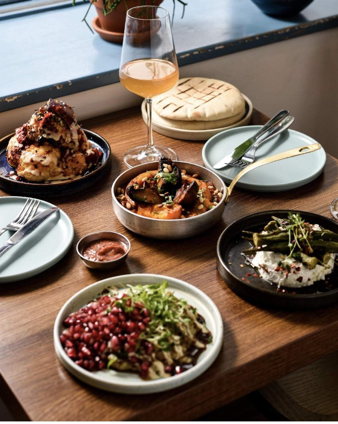 A table at Imad's Syrian Kitchen in London is topped with plates of Middle Eastern appetizers such as cauliflower, aubergine, and pita bread.