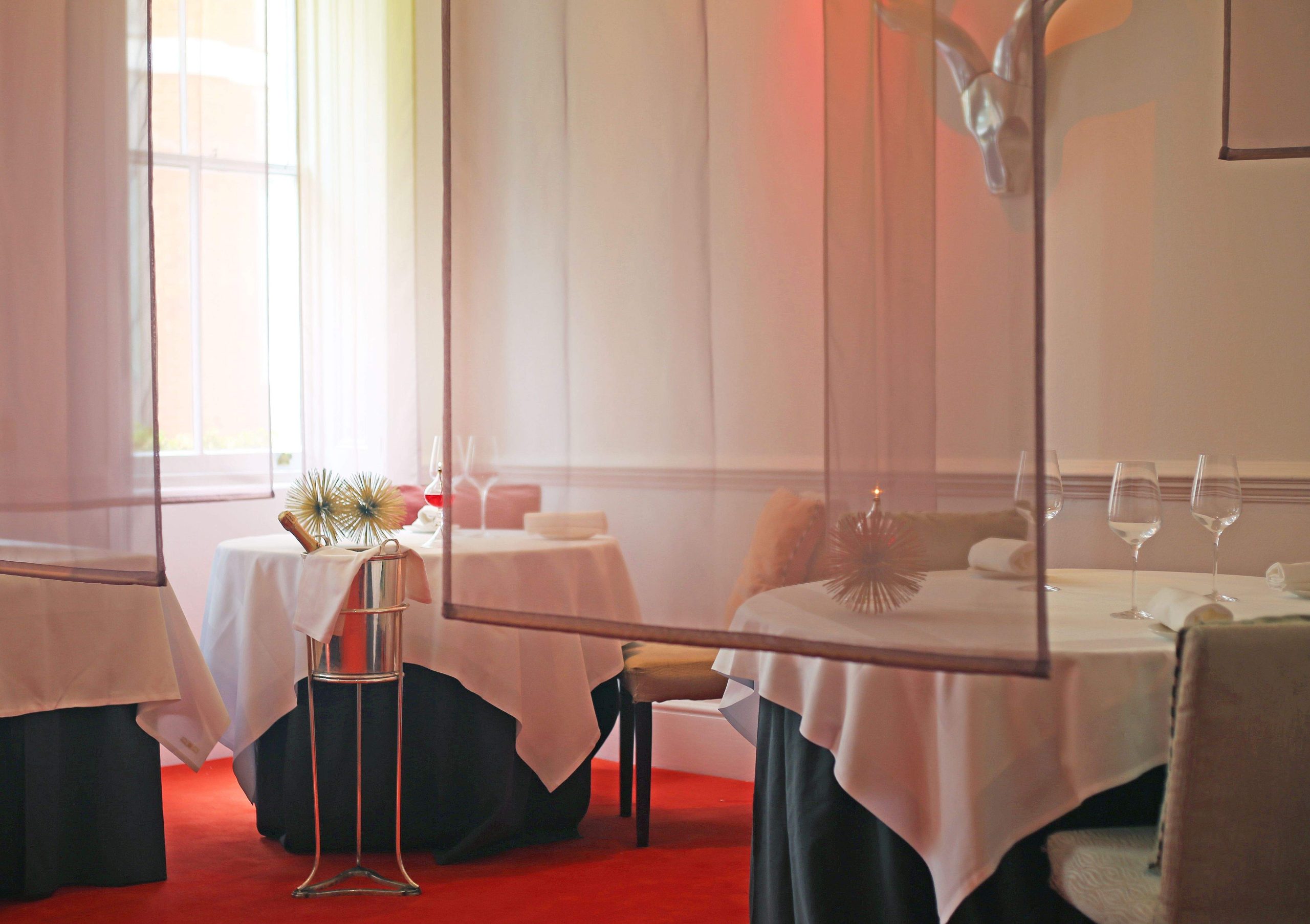 A trio of tables with blue and white tablecloths stand against a red carpet at Gauthier Soho, a restaurant in London.