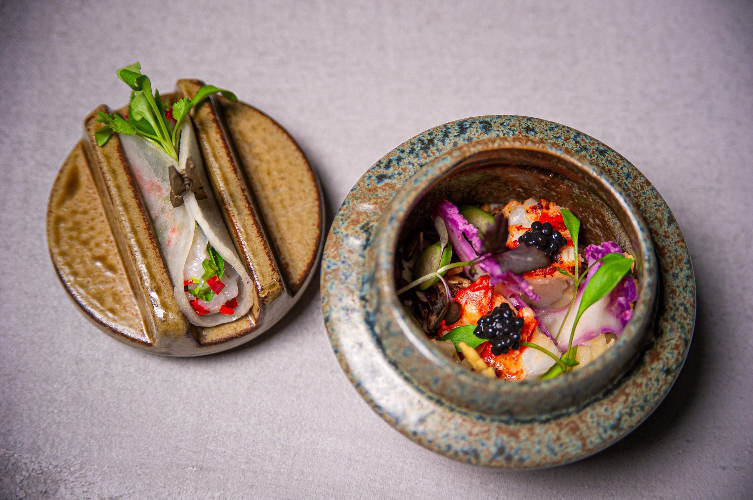 Two Indian-inspired dishes adorned with flowers and fresh herbs sit on top of a table at Opheem, a restaurant in Birmingham.