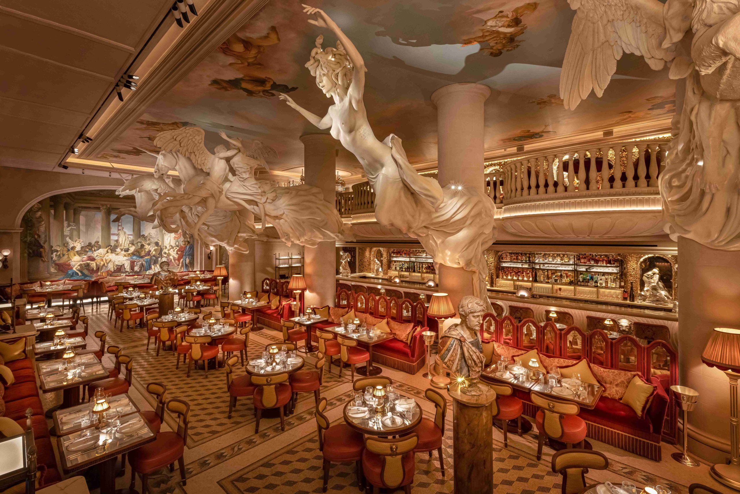 An aerial shot of the dining room at Bacchanalia, a restaurant in London, featuring red-velvet seating, ceiling frescoes, and giant sculptures suspended above tables.