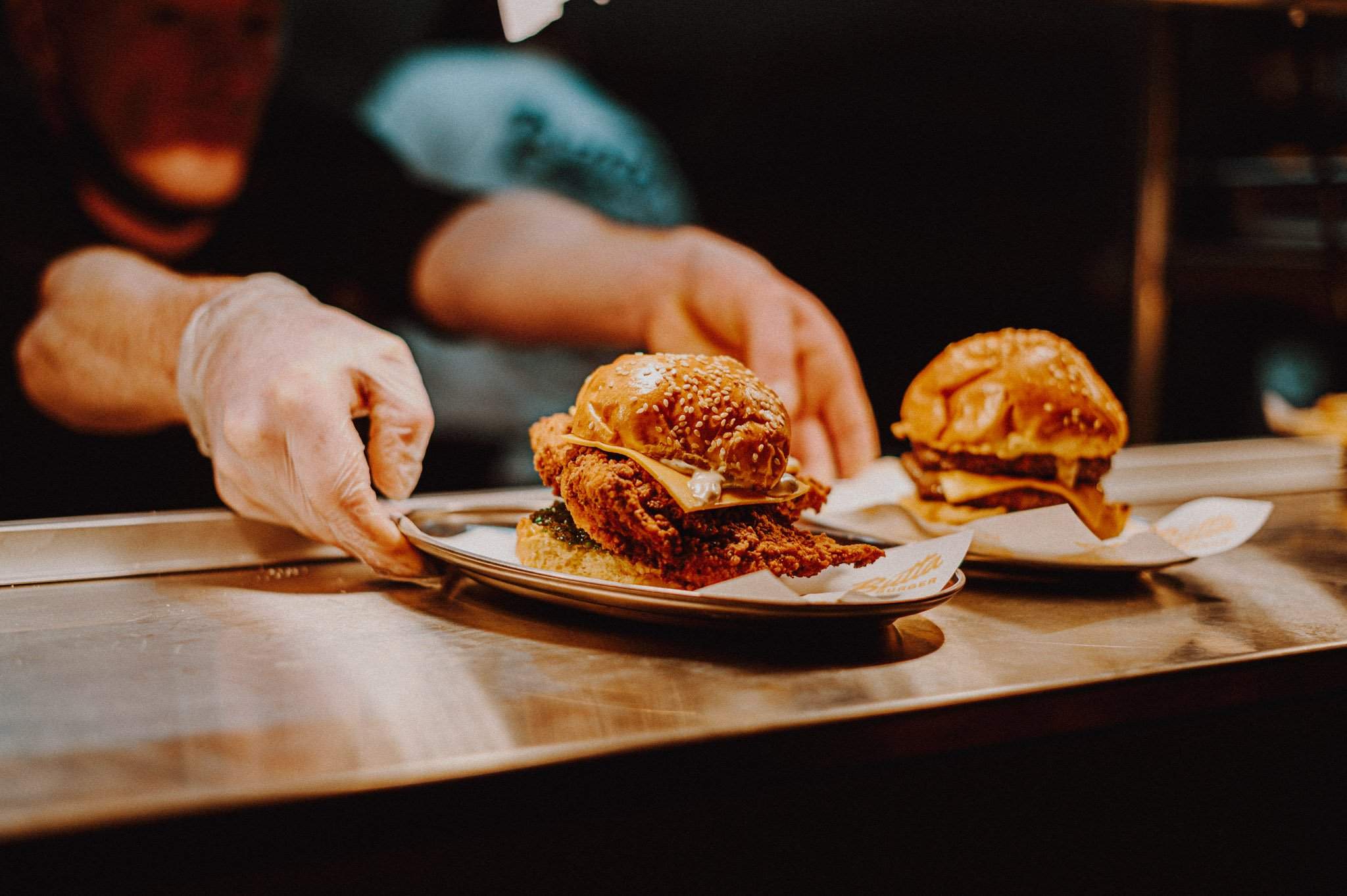 A chef hands two chicken burgers over the pass at Butta Burger, a restaurant in Edinburgh