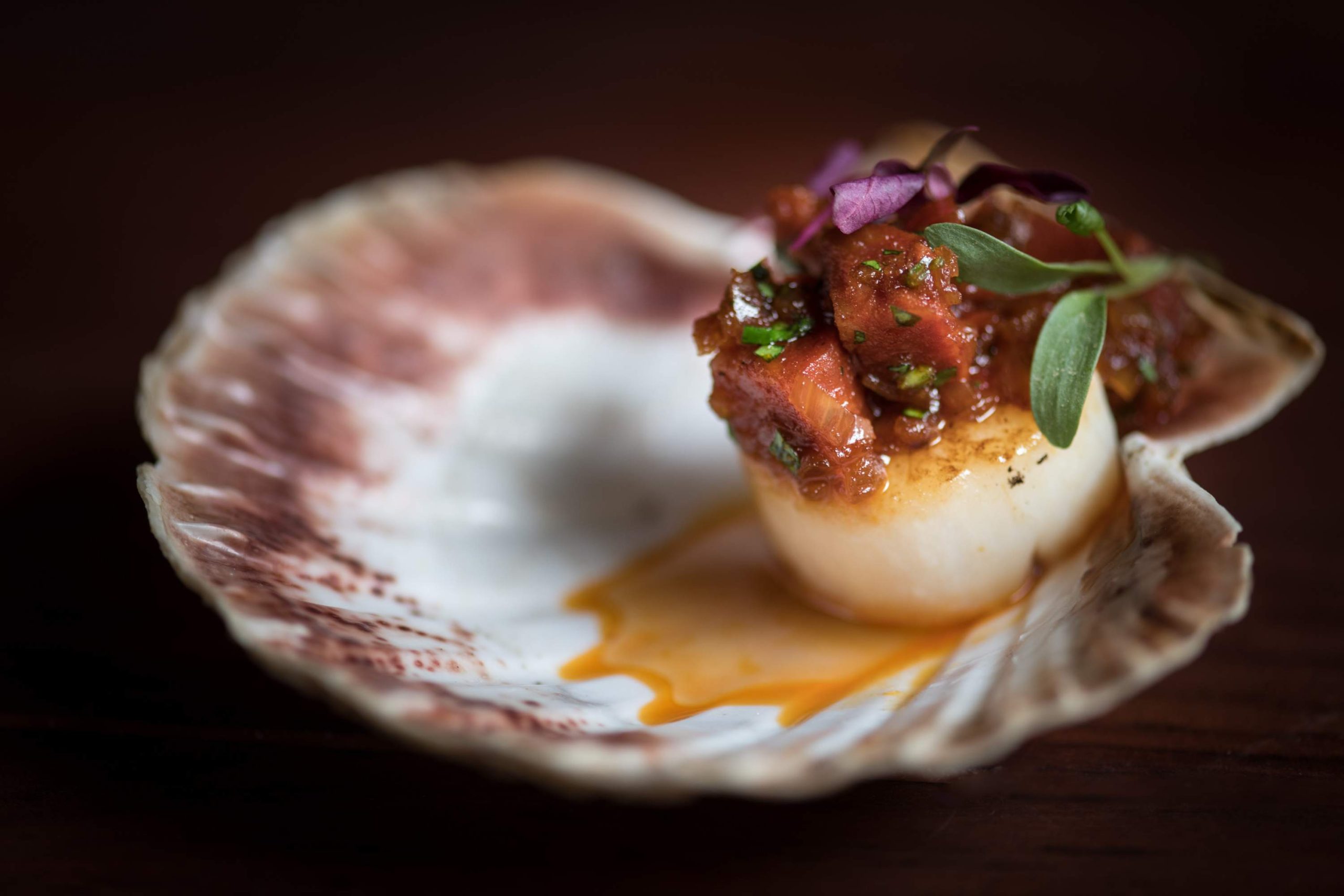 A scallop sits in its shell topped with lardons and micro herbs at Papa L’s, a restaurant in London