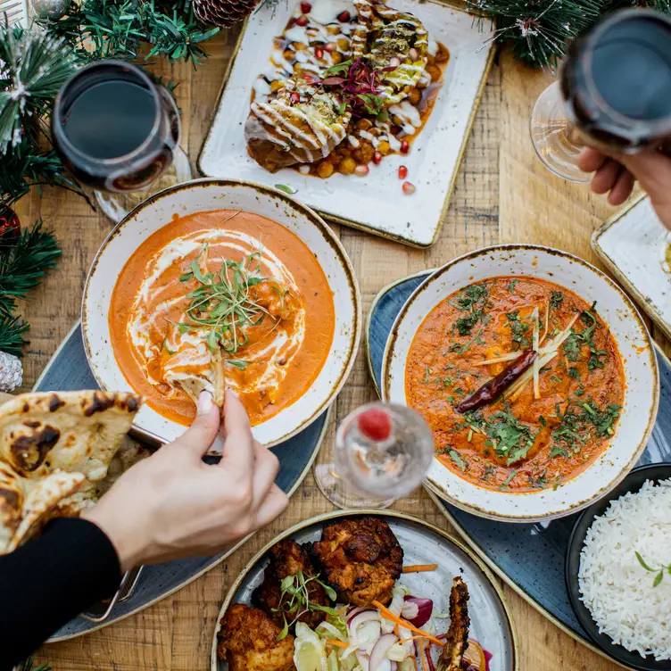 A table of curry dishes with a diner dipping a naan bread into a curry at one of the best Indian restaurants in Manchester. Credit: Delhi House Cafe