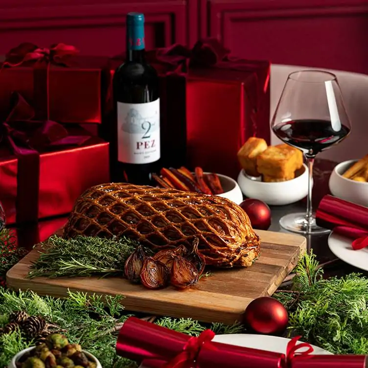 A lattice-wrapped joint of meat with all the trimmings and a bottle of red wine on a table at The Pem, one of the best restaurants in London for Christmas.