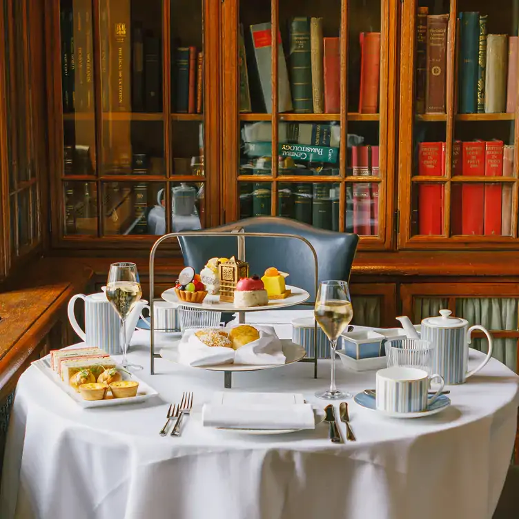 A table set with afternoon tea on a tiered platter, with glassed bookshelves behind, at The Library at County Hall, one of the best London Christmas restaurants.