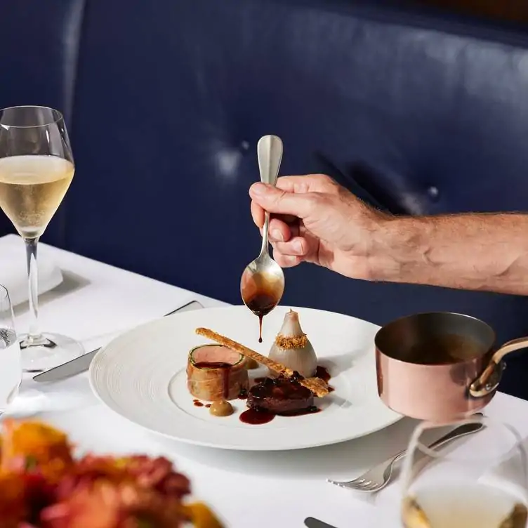 Sauce being taken from a copper pan and drizzled over an intricate dessert at Indigo at One Aldwych, one of the best London Christmas restaurants.