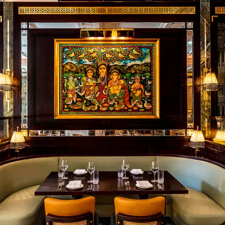 A booth table set for four people at Jamavar, one of the best festive restaurants in London, with an Indian painting on the wall.