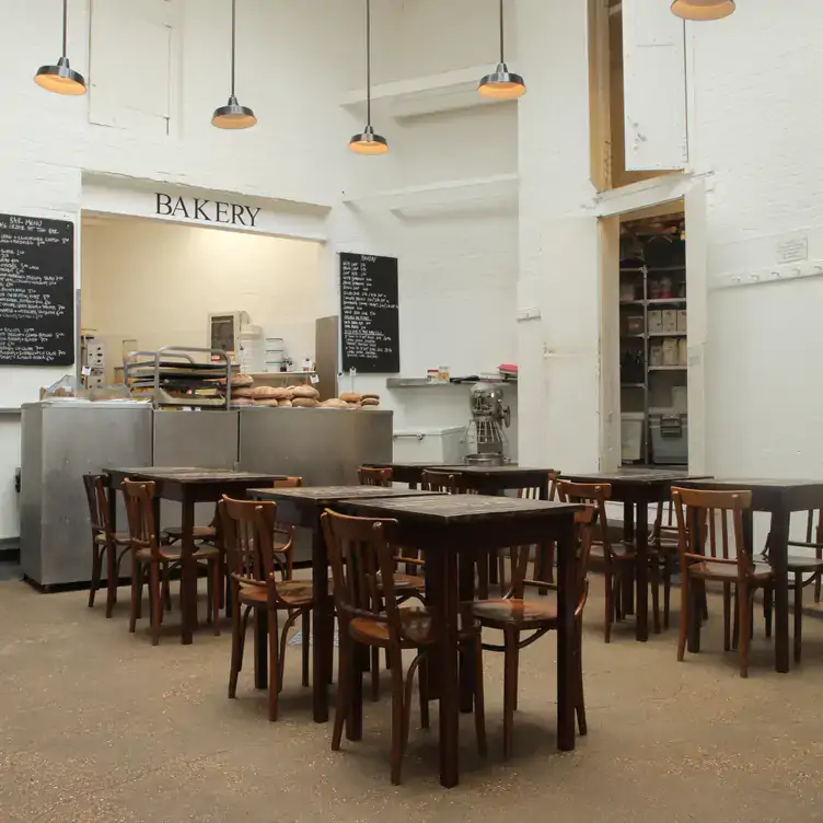 A dining area at ST. JOHN, one of the best restaurants for Christmas in London, with a bakery counter in the background and dark wood tables and chairs.