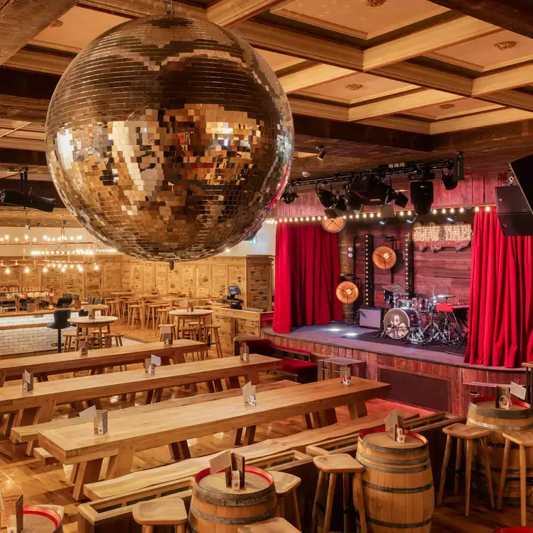 A bierkeller-style dining area at Albert’s Schloss, featuring long wooden tables, a stage with a drum kit and a mirror ball on the ceiling.