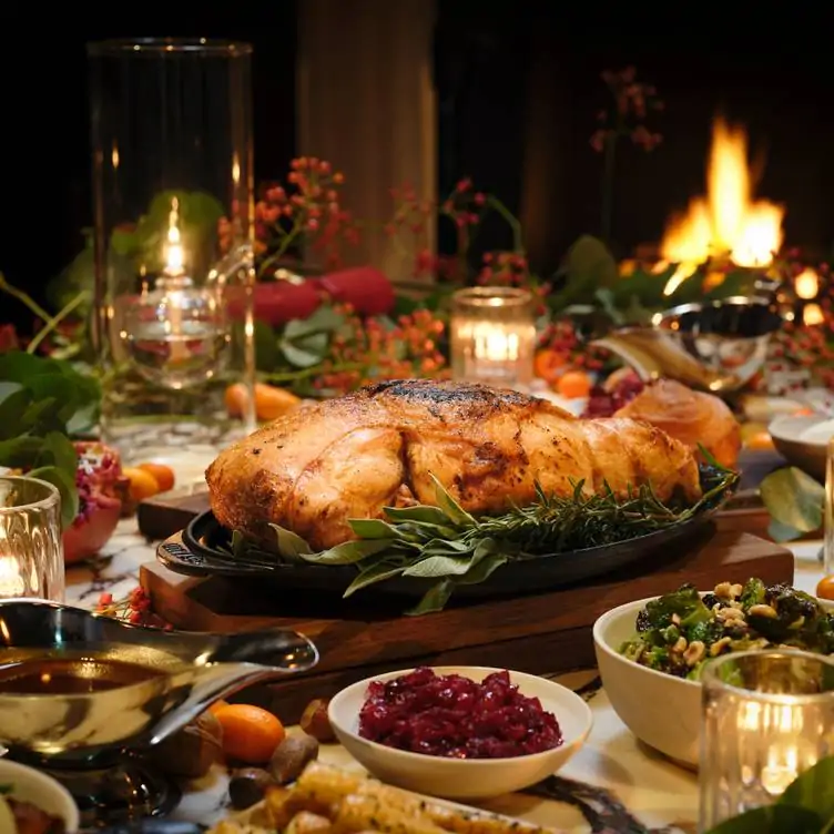 A Christmas meal designed for sharing with multiple sides and condiments, at a table set with candles in glass holders at The NoMad London.