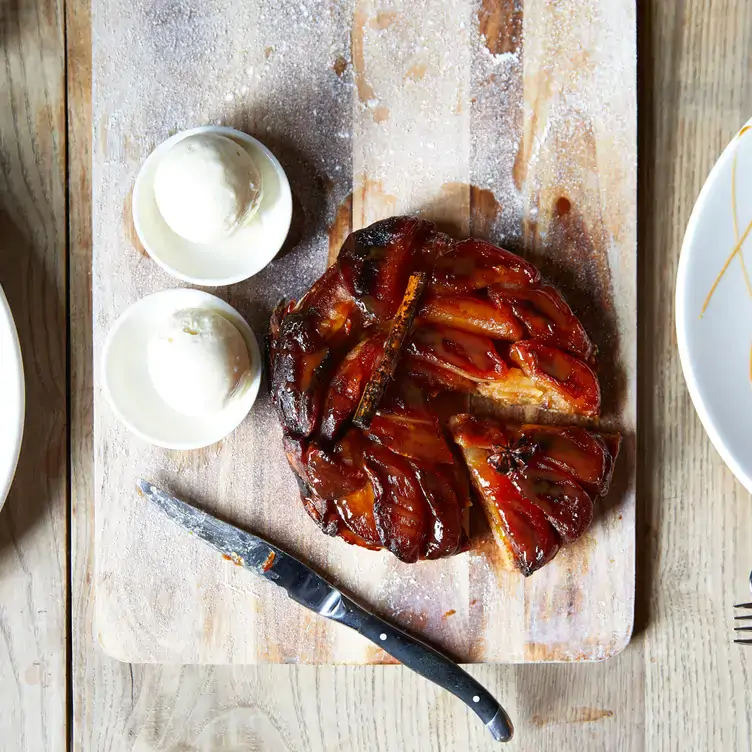 A sticky dessert with a slice being cut out and two scoops of ice cream in small dishes, on a board at The Surprise Chelsea, one of the best Christmas restaurants in London.