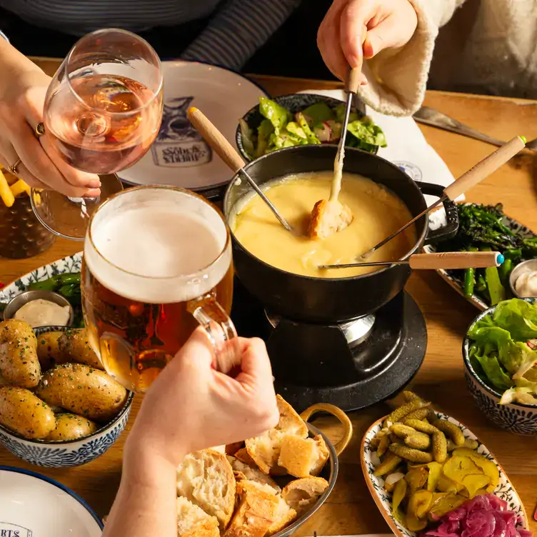 Diners clinking drinks and eating cheese fondue and other dishes at Albert’s Schloss, one of the best restaurants for Christmas in London.