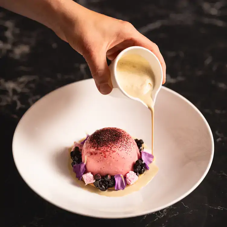 Cream is poured from a jug over a decorative purple dessert, served at The Pem, one of the best Christmas restaurants in London.