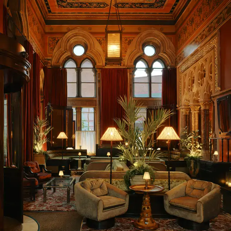 A seating area at The Midland Grand Dining Room, with comfortable armchairs grouped around low tables and low lighting from standing lamps.