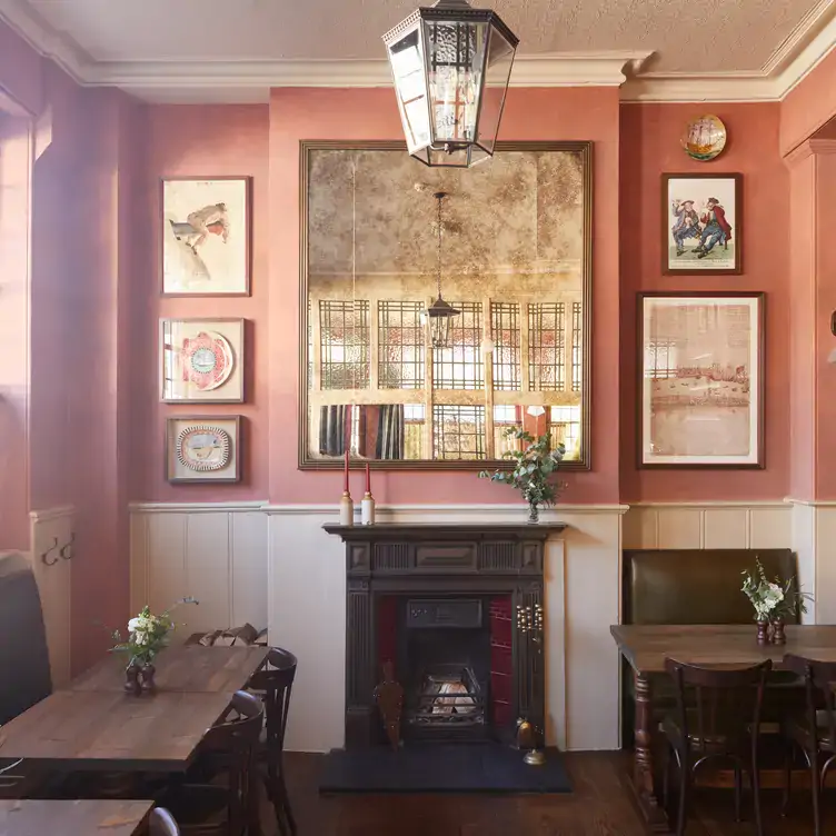 A dining area at The Surprise Chelsea, one of the best London Christmas restaurants, showing an open fireplace and warm woods with pink decor.