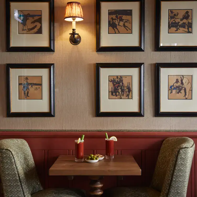 A table for two people with red cocktails on the table and artwork on the walls, at The Surprise Chelsea, one of the best festive restaurants in London.