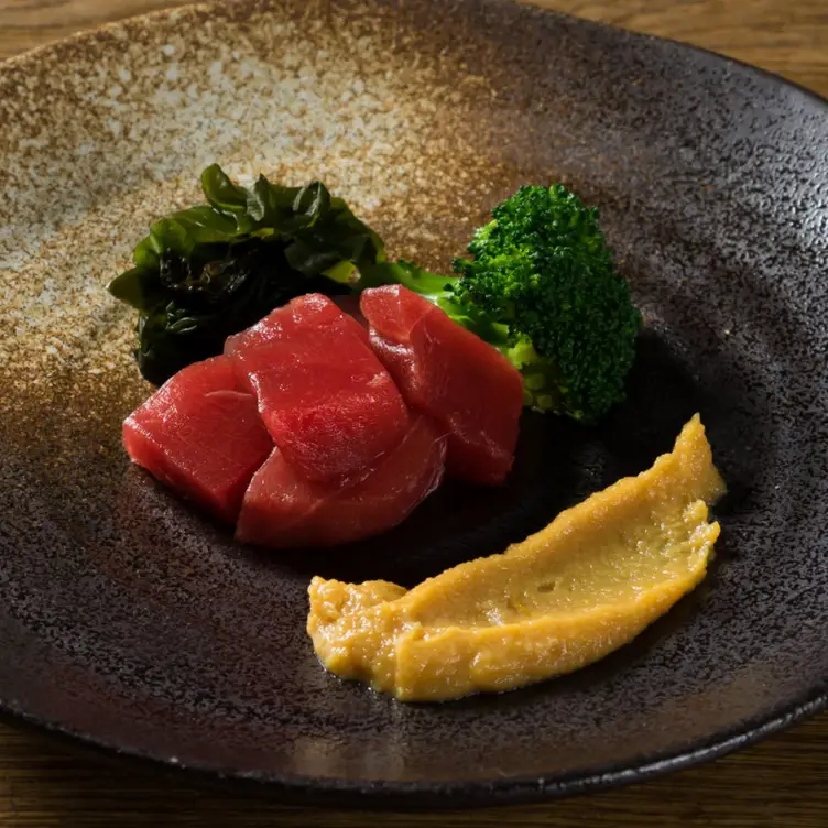 A plate of tuna sashimi with a garnish of broccoli and a yellow sauce at KIKUCHI.