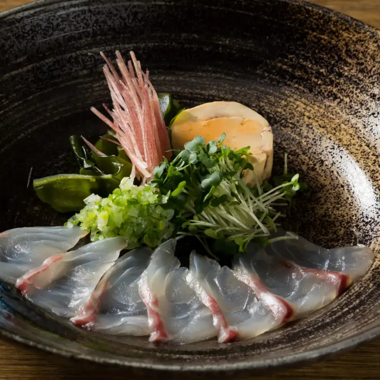 A bowl of sashimi garnished with fresh herbs at KIKUCHI.