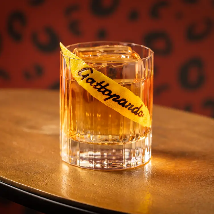 A simple cocktail in a tumbler glass with a slice of lemon peel with the restaurant logo imprinted on it at Gattopardo in London.