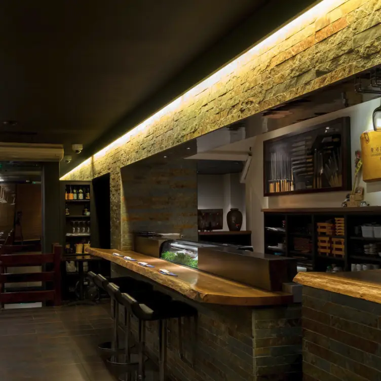 A dimly-lit setting of the restaurant interior, including stools at the sushi bar at KIKUCHI.