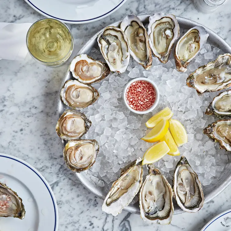 A table displaying a large plate of oysters resting on ice with slices of lemon and a glass of wine at Bibendum Oyster Bar, one of the best seafood restaurants in London.