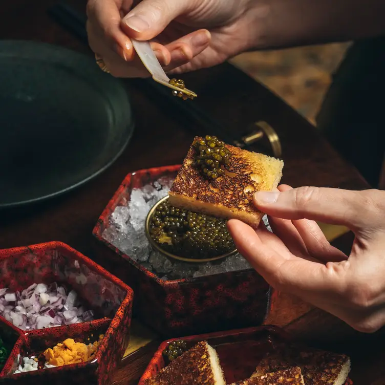 A customer holds a slice of toast with caviar in one hand and a spoon in the other at The Aubrey @ Mandarin Hotel, one of the best sushi restaurants in London.