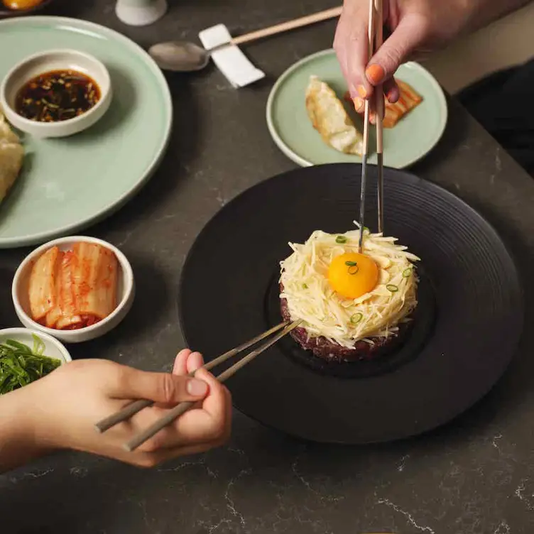 Two people leaning in with chopsticks and a meal with egg and cheese at Korean Grill Kensington.