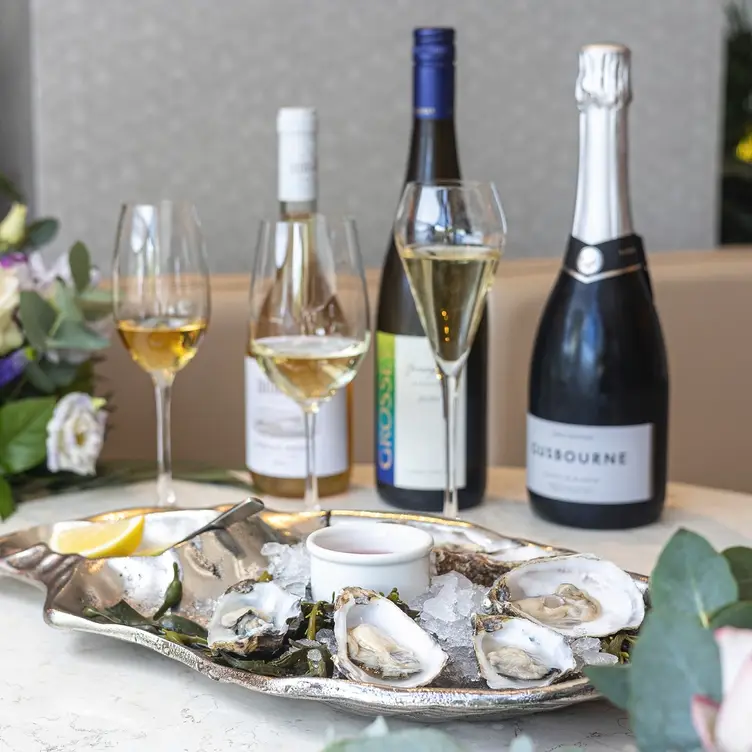 An oyster platter and wine glasses, with bottles of white wine and champagne at River Restaurant Gordon Ramsay.