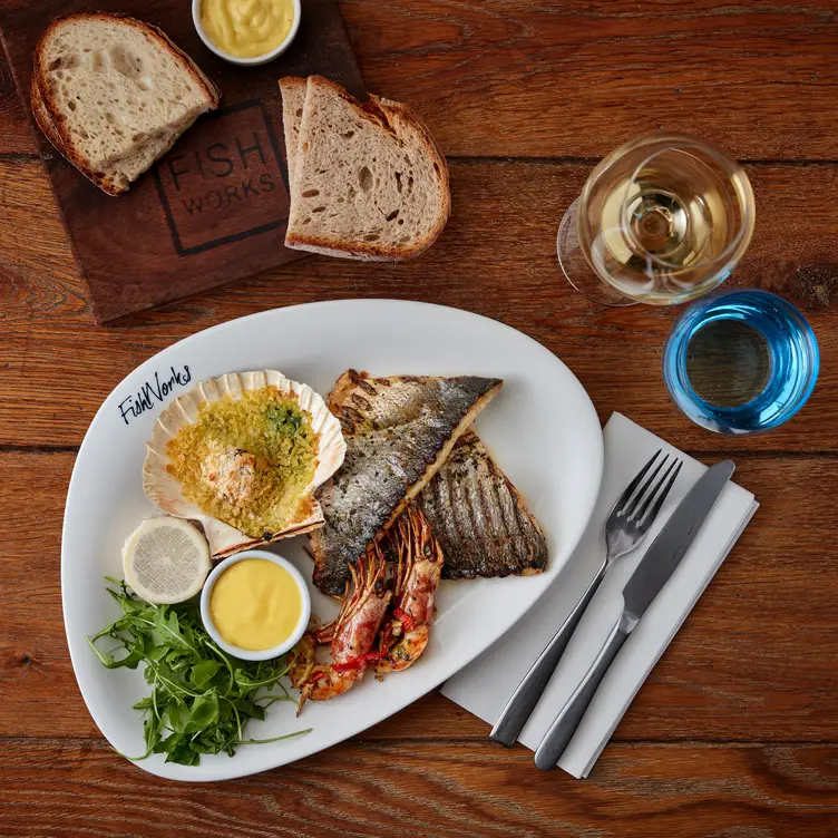 A plate of various seafood items lays on a wooden table with bread and wine at Fishworks - Covent Garden, one of the best seafood restaurants in London.