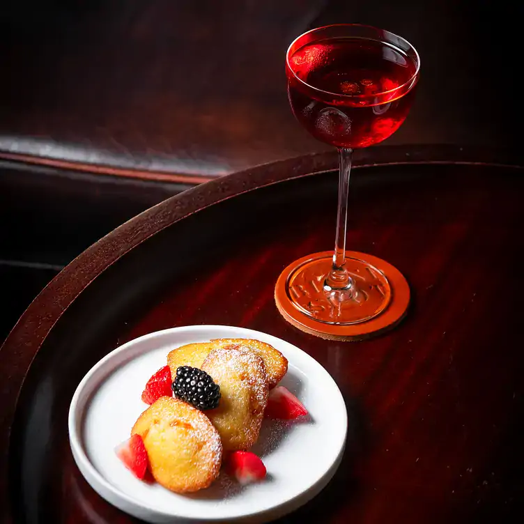 A tall red cocktail on a table with a plate of fruit and pastries at Blind Spot, one of the best romantic restaurants in London.