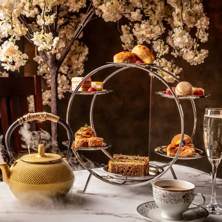 An elegant afternoon tea display, featuring tiered stands with scones, finger sandwiches, and pastries, set against blooming cherry blossoms.