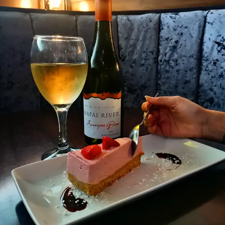 A diner cuts into a strawberry cheesecake with a bottle of wine on the side at Mharsanta, one of the best date night restaurants in Glasgow.