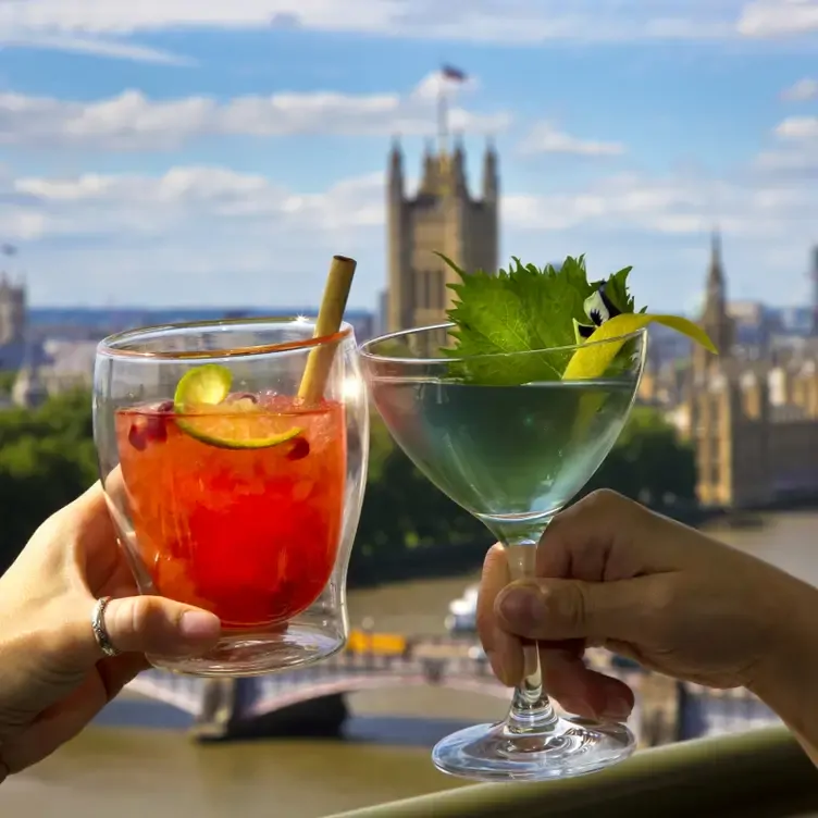 Two drinks being clinked, with London’s skyline in the background at Mezemiso, one of the best Lebanese restaurants in London.