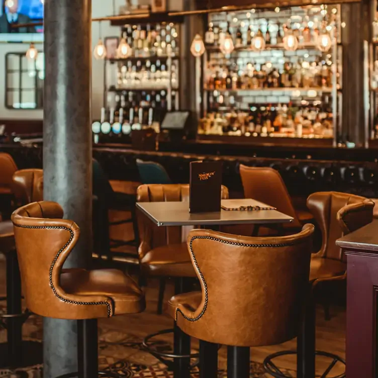 Leather backed chairs around a table, with the bar in the background at The Smokin Fox.