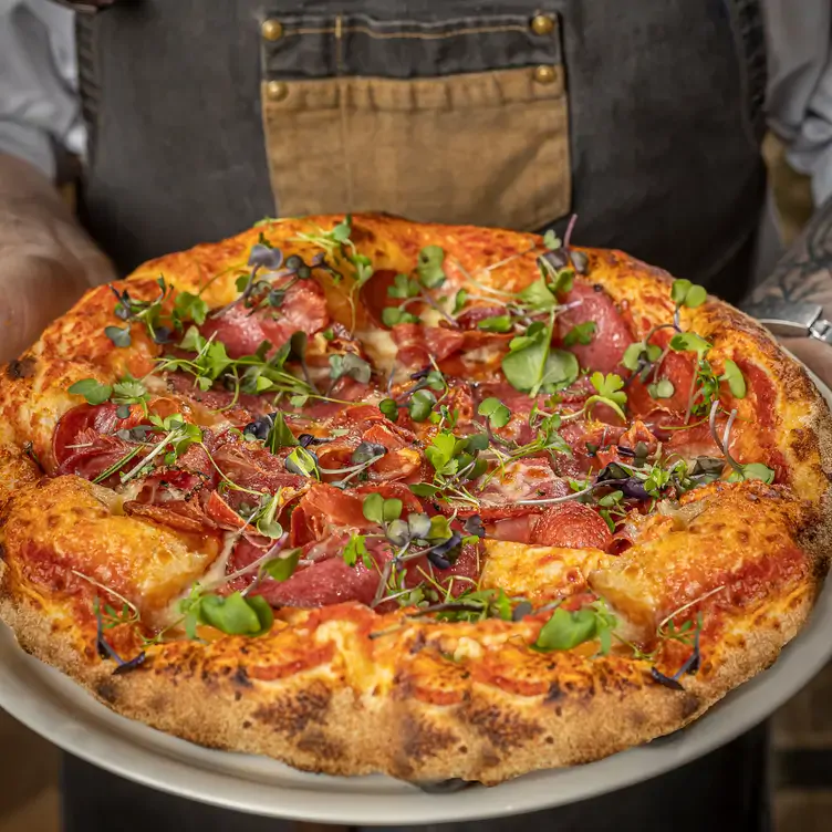 A chef holds a pizza topped with cured meat and herbs at The Black Forge, one of the best pubs in Dublin.