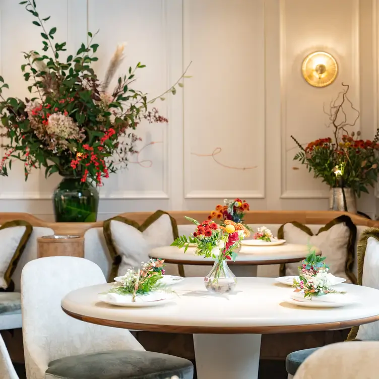 The interior of CORE by Clare Smyth. Round tables are surrounded by cushioned chairs or circular booths and the tables and walls are decorated with colourful flowers.