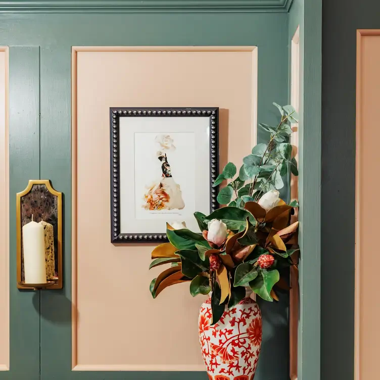 A framed painting on a pink and grey wall with flowers in a vase at The High Field, in Birmingham.